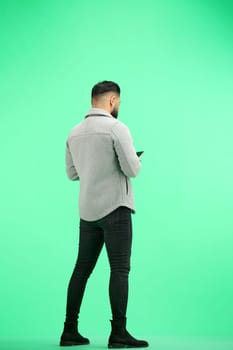 A man, full-length, on a green background, uses a phone.