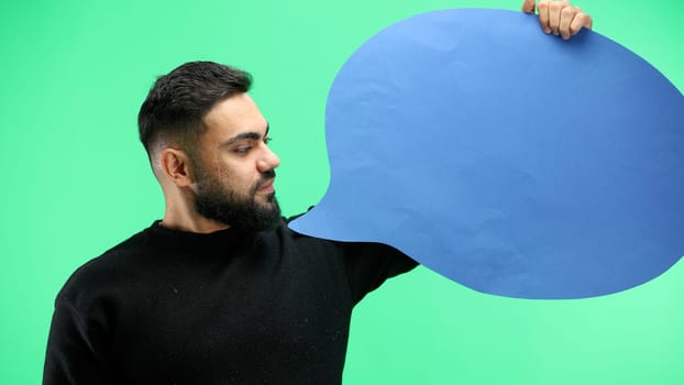 A man, close-up, on a green background, shows a blue comment sign.