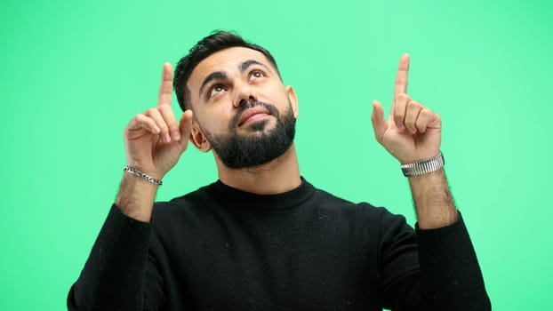 Man, close-up, on a green background, pointing up.