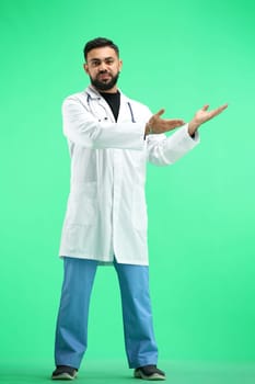 The doctor, in full height, on a green background, points to the side.