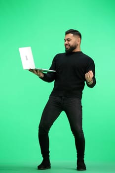A man, in full height, on a green background, uses a laptop.