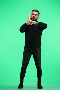 A man, full-length, on a green background, talking on the phone.