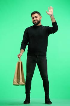 A man, full-length, on a green background, with bags, waving his hand.