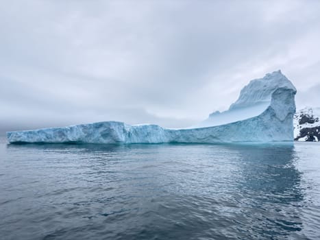 A huge high breakaway glacier drifts in the southern ocean off the coast of Antarctica at sunset, the Antarctic Peninsula, the Southern Arctic Circle, azure water, cloudy weather. High quality photo