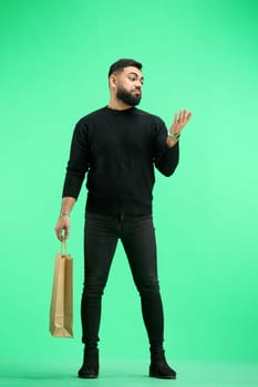 A man, full-length, on a green background, with bags, points to the side.