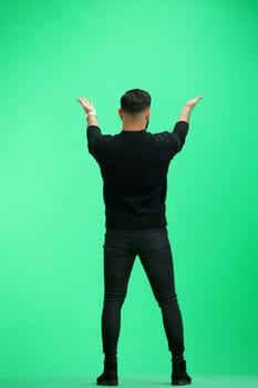 A man, full-length, on a green background, spreads his arms.