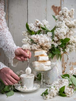 woman preparing a cold coffee dessert, spring still life in retro style, a stack of waffle ice cream in a bowl with a bouquet of white lilacs in an antique teapot, high quality photo