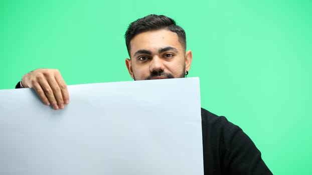 A man, close-up, on a green background, shows a white sheet.