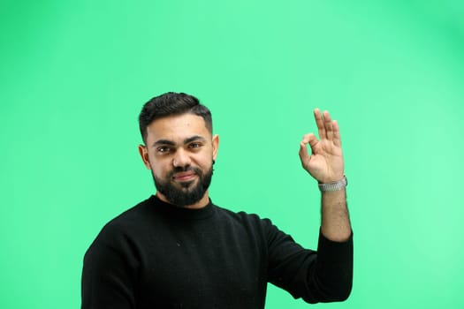 A man, close-up, on a green background, shows an ok sign.
