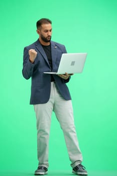 A man, full-length, on a green background, uses a laptop.