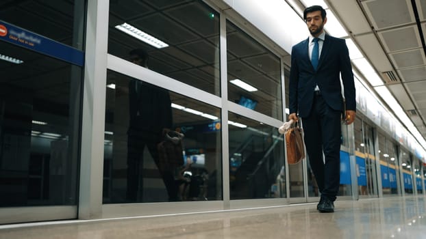 Smart executive manager walking along at train while holding bag and headphone.Handsome attractive business man going back to home at train station.Expert investor using public transport. Exultant.