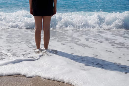 bare feet of a girl in a black T-shirt in the sea foam on the beach in sunlight