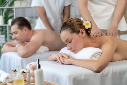 Caucasian couple customer enjoying relaxing anti-stress spa massage and pampering with beauty skin recreation leisure in day light ambient salon spa at luxury resort or hotel. Quiescent