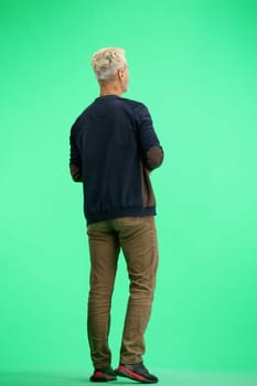 A man, full-length, on a green background, uses a phone.