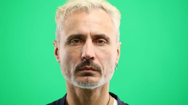 Man's face, in close-up, on a green background.