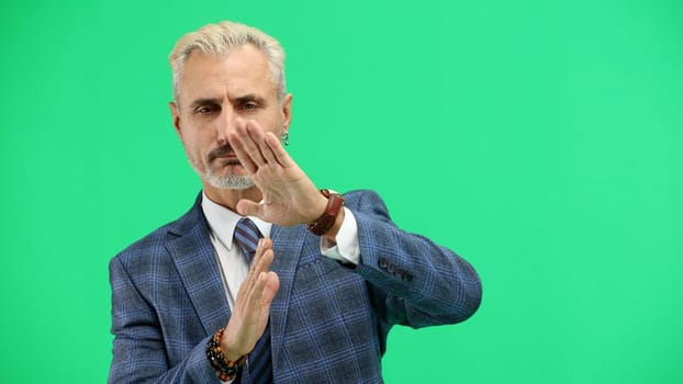 A man, close-up, on a green background, shows a pause sign.