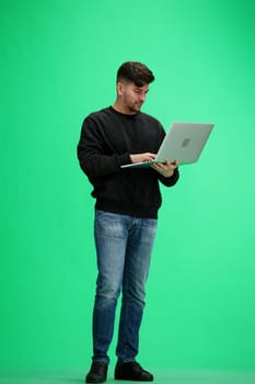 A man, full-length, on a green background, uses a phone.