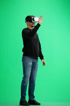 A man, full-length, on a green background, listening to music with headphones.