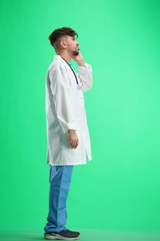 The doctor, in full height, on a green background, talking on the phone.