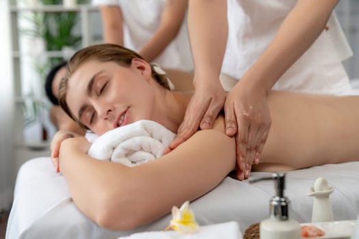 Caucasian couple customer enjoying relaxing anti-stress spa massage and pampering with beauty skin recreation leisure in day light ambient salon spa at luxury resort or hotel. Quiescent