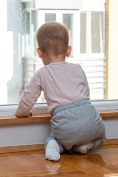 A child stands near an apartment window, looking with a mixture of hope and melancholy at the building outside, dreaming of a walk in the open air. Concept of loneliness and desire for exploration