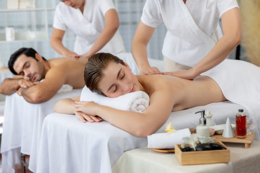 Caucasian couple customer enjoying relaxing anti-stress spa massage and pampering with beauty skin recreation leisure in day light ambient salon spa at luxury resort or hotel. Quiescent