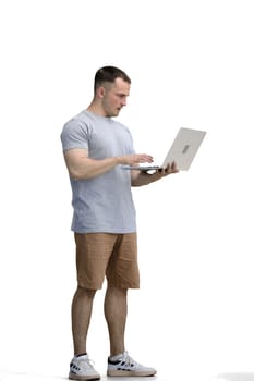 A man in a gray T-shirt, on a white background, in full height, uses a laptop.