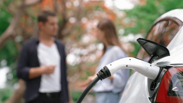 EV car recharging electricity for battery by lovey couple traveling during their road trip travel by eco friendly electric vehicle in national park autumnal forest on holiday. Exalt