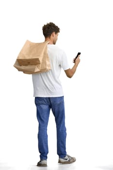 A man in a white T-shirt, on a white background, full-length, with bags and a phone.