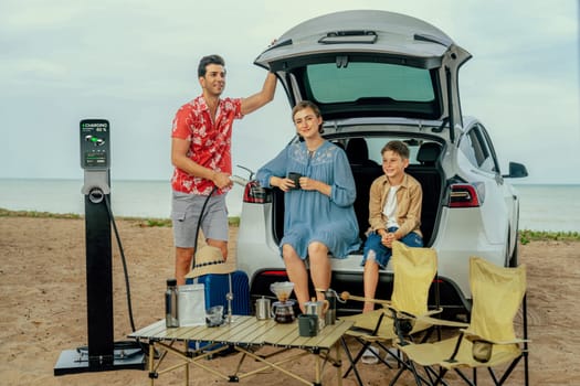 Family vacation trip traveling by the beach with electric car, happy family recharge EV car, enjoying outdoor camping coffee. Seascape travel and eco-friendly car for clean environment. Perpetual