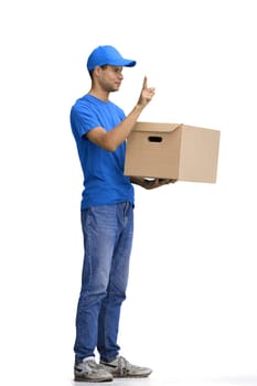 A male deliveryman, on a white background, in full height, with a box, shows an important sign.