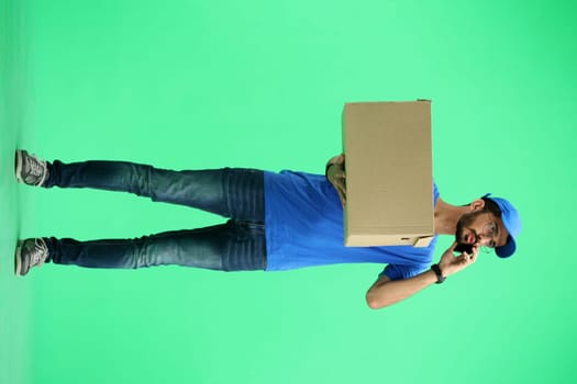 A male deliveryman, on a green background, in full height, with a box and a phone.