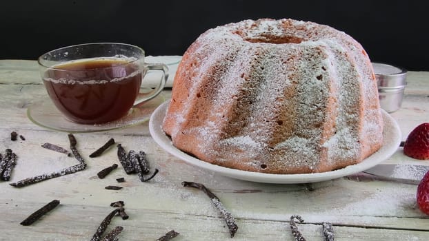 Old fashioned sand cake with cup of black tea and pieces of vanilla on wooden background. Egg-yolk sponge cake with stawberries on rustic white background.