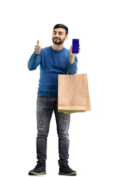 A man, full-length, on a white background, with bags, shows a phone.