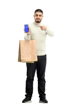 A man, full-length, on a white background, with bags, shows a phone.