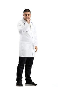 The doctor, in full height, on a white background, shows a sign of silence.
