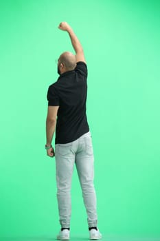A man, on a green background, in full height, raised his hand.