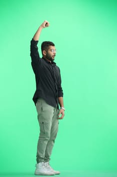 A man, on a green background, in full height, raised his hand.