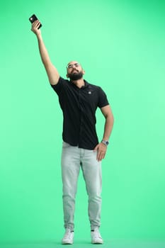 A man, on a green background, in full height, waving his phone.