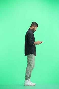 A man, on a green background, in full height, with a phone.