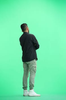 A man, on a green background, in full height, crossed his arms.
