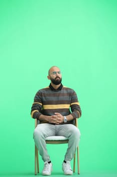 A man, on a green background, is sitting on a chair.