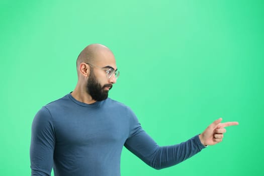 A man, on a green background, in close-up, points to the side.