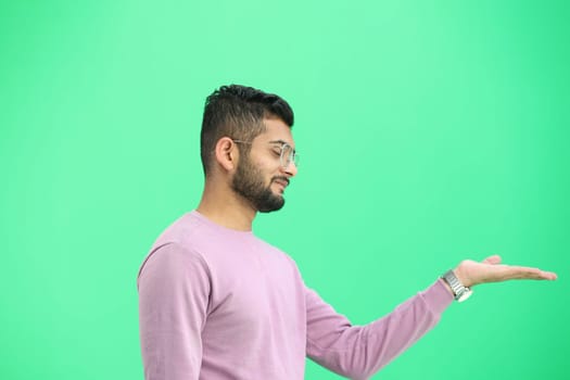 A man, on a green background, in close-up, points to the side.
