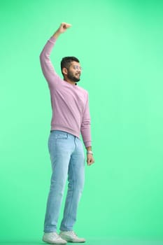 A man, on a green background, in full height, raised his hand.