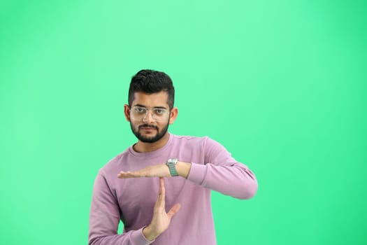 A man, on a green background, in close-up, shows a pause sign.