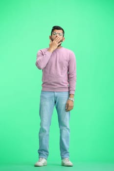 A man, on a green background, in full height, yawns.