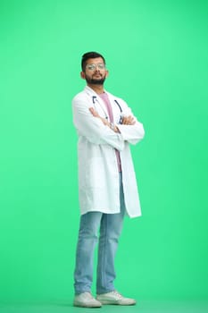 The male doctor, on a green background, in full height, crossed his arms.