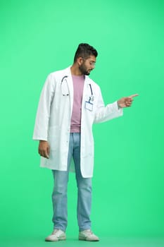 The male doctor, on a green background, in full height, points to the side.