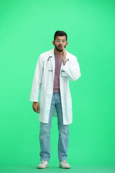 A male doctor, on a green background, in full height, tells a secret.